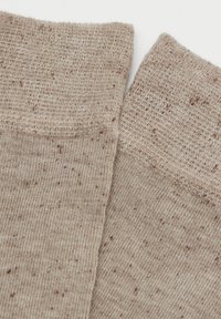 Beige strikkede sokker med et struktureret, spraglet mønster i mørkere brun. Har ribbede kanter og et blødt, let materiale.