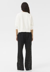 White cropped sweater with long sleeves paired with loose-fitting black lace pants featuring a floral pattern and sheer texture.