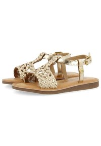 Goudkleurige gevlochten sandalen hebben een T-bandontwerp, gladde leren accenten en een duurzame rubberen zool. Verstelbare enkelgesp voor een veilige pasvorm.