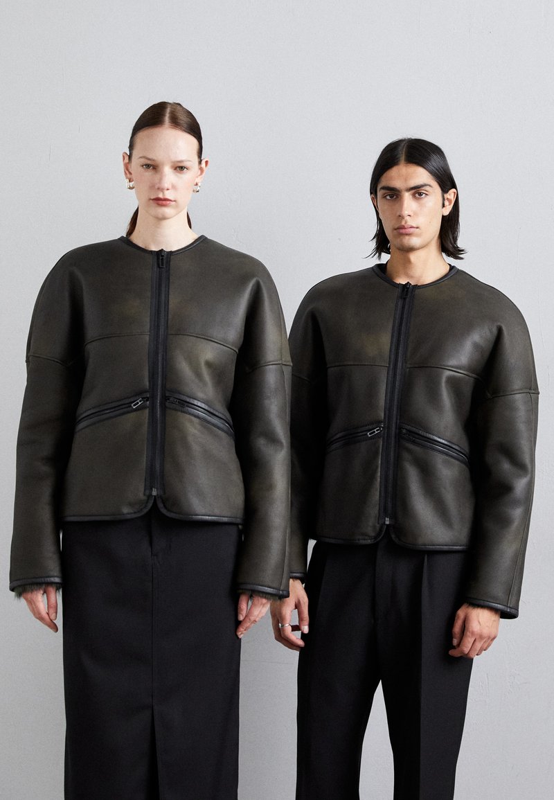 Dunkelgrüne Lederjacke mit strukturiertem Design, ausgestattet mit einem Reißverschluss auf der Vorderseite und horizontalen Reißverschlusstaschen. Glatte Textur und taillierte Passform.