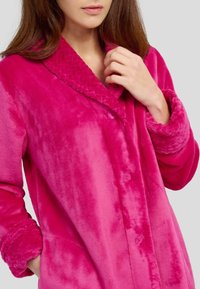 Bata de baño de forro polar en un vibrante color rosa, con un cuello texturizado, cierre de botón y puños de felpa, con bolsillos laterales y una textura suave y lisa.