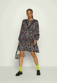 Vestido com estampa floral, mangas bufantes longas, detalhes em preto e saia drapeada, combinado com uma mala com estampa de zebra e meias verde néon.