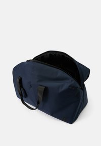 Navy blå duffelbag med en glat, mat finish. Har dobbelte sorte håndtag og en lynlåsåbning til et rummeligt indre.