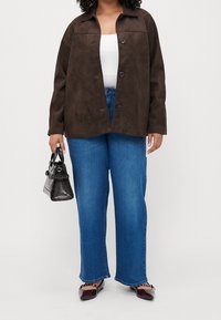 Hnědá semišová bunda s límcem, předním zapínáním na knoflíky, dlouhými rukávy; ve spojení s modrými džínami se širokými nohavicemi a černou kabelkou.
