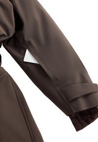 Hnedý, vodoodpudivý rukáv bundy so štruktúrovanou tkaninou, manžeta so strapcom a bočná vrecko, v ktorom je biela karta.