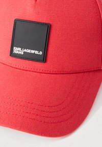 Boné de tecido texturizado vermelho com um remendo quadrado preto com a marca branca "KARL LAGERFELD JEANS" no painel frontal.