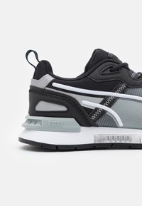 Black and gray sneaker with a textured mesh upper, synthetic accents, and white detailing. Features a cushioned sole and pull tab at the heel.