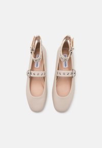 Beige Mary Jane schoenen met een afgeronde neus, een band met zilveren studs en een gespsluiting. Gemaakt van soepel synthetisch materiaal.