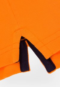 Pomarańczowy materiał o teksturowanej powierzchni, z granatowym kontrastem na brzegach oraz V-kształtnym rozcięciem dla dodatkowego detalu projektowego.