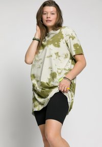 Oversized tie-dye T-shirt in cream and olive; features short sleeves, round neckline, and side slits. Paired with black cycling shorts.
