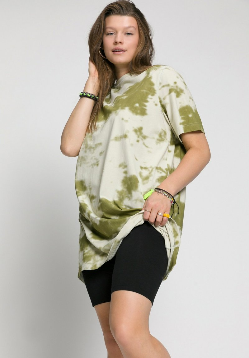 Oversized tie-dye T-shirt in cream and olive; features short sleeves, round neckline, and side slits. Paired with black cycling shorts.