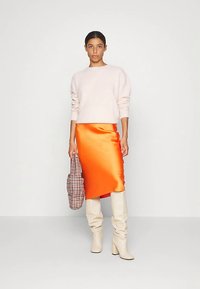 Világos rózsaszín pulóver, narancssárga szatén szoknya, bézs térdig érő csizma és egy kockás táska. Simaság érzetű anyagok, kontrasztos színek és elegáns sziluett.