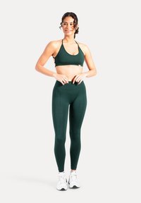 Mörkgröna sport-bh och höga leggings i set. Bh:n har tunna axelband och logotypdetalj; leggingsen har en slät yta och subtilt mönster.
