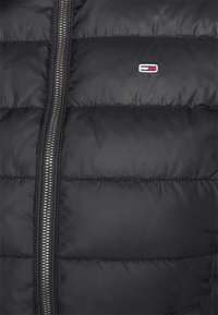 Czarna pikowana kurtka z zamkiem błyskawicznym, z małym logo w kolorach czerwonym, białym i niebieskim. Gładka tekstura i pikowane wzornictwo. Srebrne okucia zamka.