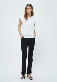 Camiseta blanca de manga corta combinada con pantalones negros ajustados. La camiseta presenta un escote redondo; los pantalones tienen una textura suave y un corte recto.