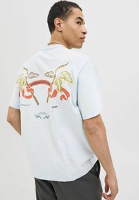Lichtblauw T-shirt met korte mouwen, voorzien van een grafisch ontwerp van palmbomen en een strik met tekst op de achterkant. Zacht katoen materiaal.