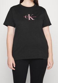 Černé bavlněné tričko s krátkým rukávem, s růžovým logem "Calvin Klein Jeans" v stylizovaném písmu uprostřed hrudi.