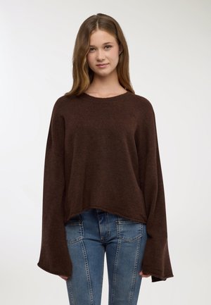 Maglione marrone oversize in maglia con scollo rotondo e maniche larghe a campana. Abbinato a jeans blu aderenti con un design a pannelli.