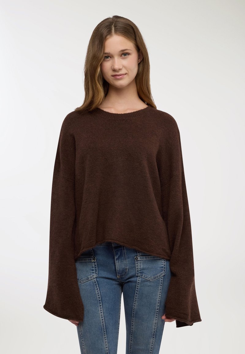 Maglione marrone oversize in maglia con scollo rotondo e maniche larghe a campana. Abbinato a jeans blu aderenti con un design a pannelli.