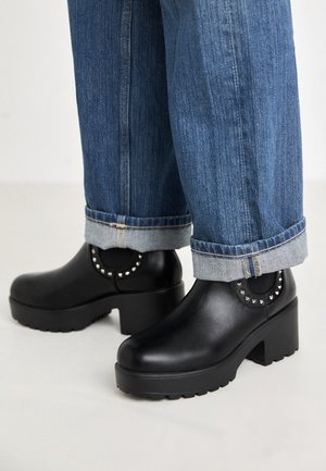 Sorte ankelstøvler med hæl lavet af glat materiale med rundet tå, tekstureret sål og nittebesætning på ankelområdet.