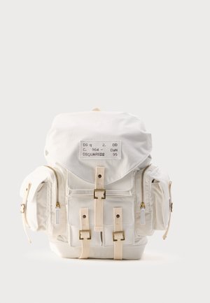 Weißer Stoffrucksack mit mehreren Reißverschlusstaschen, verstellbaren Gurten mit Schnallen und einem Patch-Label auf der oberen Klappe.