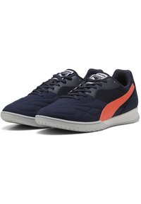 Zapatillas de deporte azul marino con textura acolchada, franja de acento naranja y secciones de malla negra. Con suela de goma con agarre estampado.