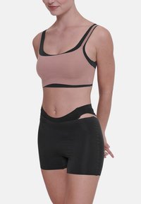 Lichte sportbeha in het roze met zwarte afwerkingen, voorzien van een ronde hals en brede bandjes. Zwarte high-waisted shorts met zijopeningen.