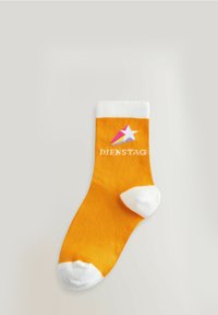 Calcetín amarillo con un puño y punta blancos, con un diseño de estrellas rosas y blancas y la palabra "DIENSTAG" impresa en blanco.
