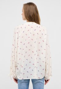 Blusa leggera in crema con stampa paisley in rosso e blu. Presenta maniche lunghe con polsini arricciati e una vestibilità morbida.