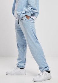 Light blue tracksuit with a subtle pattern, featuring elastic cuffs and pockets on both the jacket and pants, paired with white sneakers.