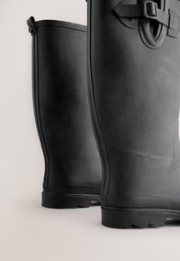 Sorte gummistøvler med glat tekstur, afrundet form og spænde-detalje nær toppen, med slidstærk sål for godt greb.