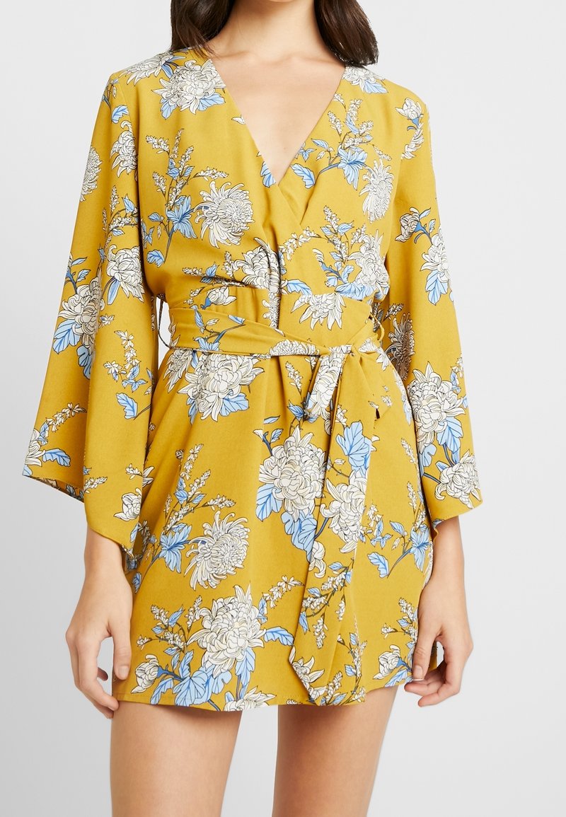 Gelbes Wickelkleid mit langen Glockenärmeln, verziert mit blauen und weißen Blumenmustern, einem tiefen V-Ausschnitt und einer Taillenbindung.