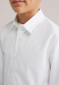 Cămașă albă cu mâneci lungi, cu nasturi, având un guler ascuțit și o textură subtilă, cu nasturi vizibili pe toată lungimea frontală.