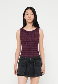 Μπορντό αμάνικο τοπ με υφή και ριχτή σχεδίαση, συνδυασμένο με μαύρη τζιν φούστα με ψηλή μέση, που διαθέτει μεγάλες μπροστινές τσέπες και κλείσιμο με κουμπί.