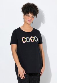 Camiseta negra de manga corta con "COCO" en adornos florales y de strass. Tela suave, corte relajado, combinada con pantalones de lunares.