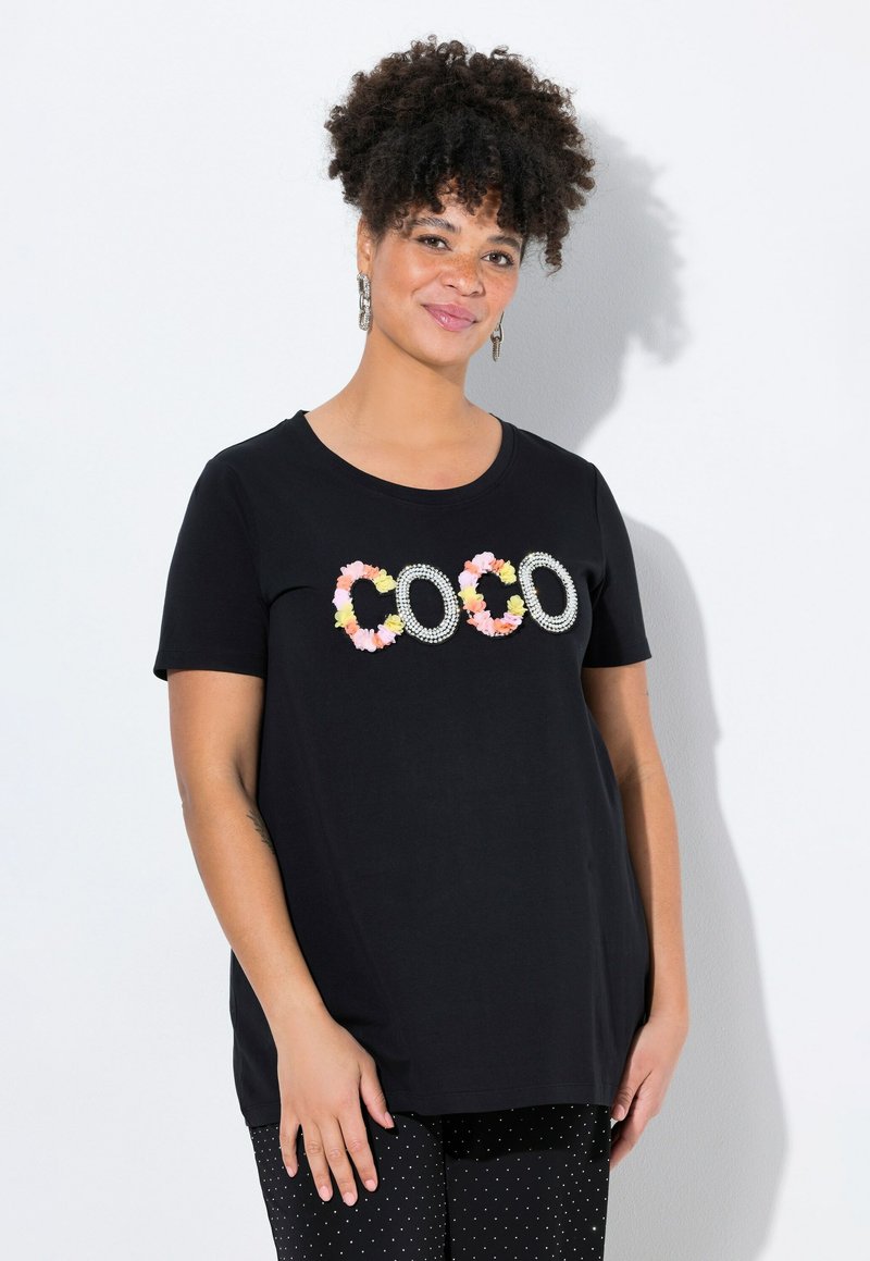 Camiseta negra de manga corta con "COCO" en adornos florales y de strass. Tela suave, corte relajado, combinada con pantalones de lunares.