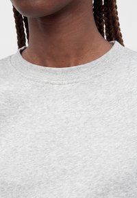 Gros plan d'une personne portant un t-shirt gris clair à col rond avec des cheveux tressés visibles derrière le cou.