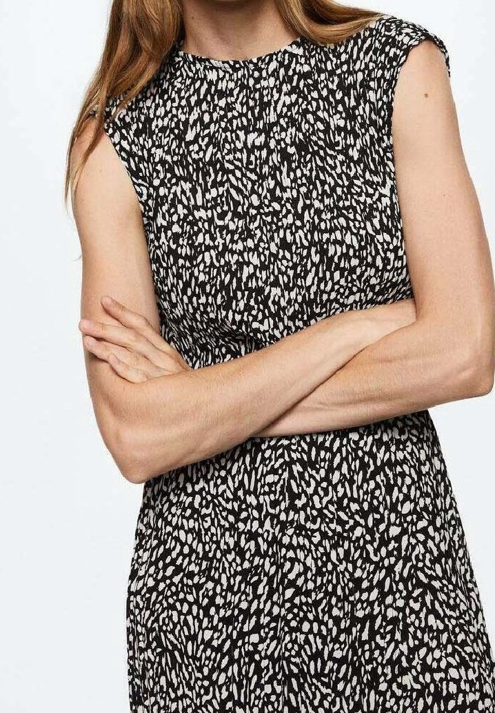 Robe à motifs noir et blanc avec des manches courtes, dotée d'un col rond et d'un tissu texturé et fluide. Bras croisés devant.