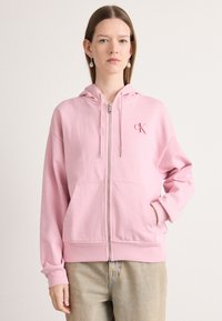 Hoodie rosa con zip in tessuto morbido, con cappuccio regolabile, tasche a marsupio e logo ricamato sul lato sinistro del petto. Vestibilità casual con polsini a coste.