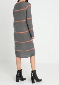 Grå stickad klänning med horisontella korallränder, långa ärmar och midiklängd, i kombination med blanka svarta ankelstövlar.