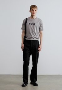 Hall hall T-särk, millel on musta värviga trükitud "BOSS", kombineeritud mustade cargo-pükstega. Komplekti kuuluvad stiilsed saapad ja õlakoti rihm.