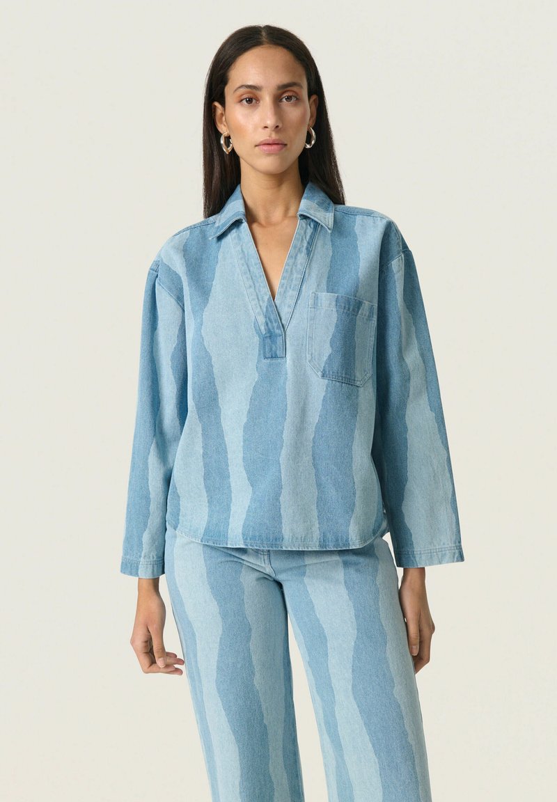 Denim shirt met een V-hals, lange mouwen en een borstzak. Kenmerkt een lichtblauwe verloopstrepenpatroon. Zachte textuur en relaxte pasvorm.
