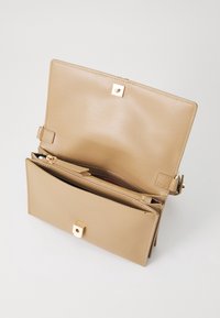 Beżowa skórzana torebka o strukturalnym fasonie, wyposażona w wewnętrzną kieszeń na suwak oraz złote kwadratowe zapięcie.