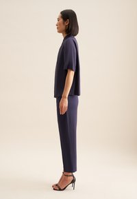 Completo due pezzi navy composto da una maglietta a maniche corte e pantaloni slim-fit, realizzato in un tessuto liscio, abbinato a sandali con tacco alto neri.