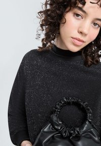 Zwarte sweatshirt met glinsterende textuur en hoge hals, gecombineerd met een kleine zwarte leren tas met een geplooide handvat.