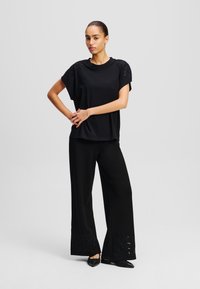 Zwarte top met korte mouwen en geborduurde schouderaccenten, gecombineerd met losse zwarte broek met bloemen uitsnijdingen aan de zoom.