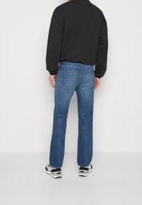 Vaqueros de mezclilla azul con corte de pierna recta, que cuentan con bolsillos traseros y un acabado desgastado. Combinados con una sudadera negra y zapatillas blancas y negras.