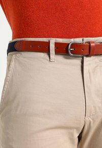 Beiga byxor med rak passform, med ett brunt läderbälte med en silvermetallspänne och marinblå textilaccent.