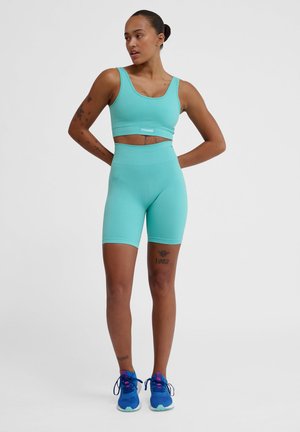 Turkis atletisk sæt med en tætsiddende cropped top og højhælede shorts. Har ribbet tekstur og en logo elastik. Blå løbesko inkluderet.