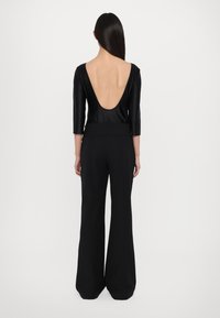 Bodysuit negro con un escote en la espalda profundo, mangas de tres cuartos combinado con pantalones anchos de cintura alta en negro. Material suave y corte entallado.